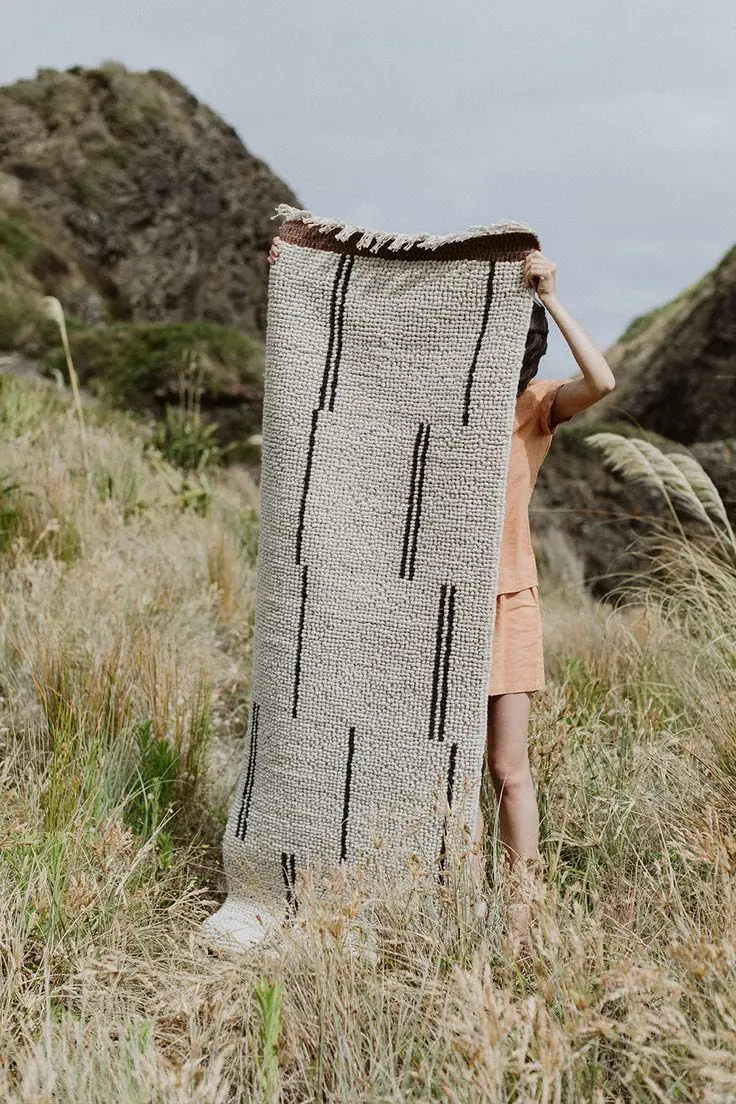 Alfombra tejida a mano, de lana cruda con líneas negras, sostenida en el campo — Hilando Culturas