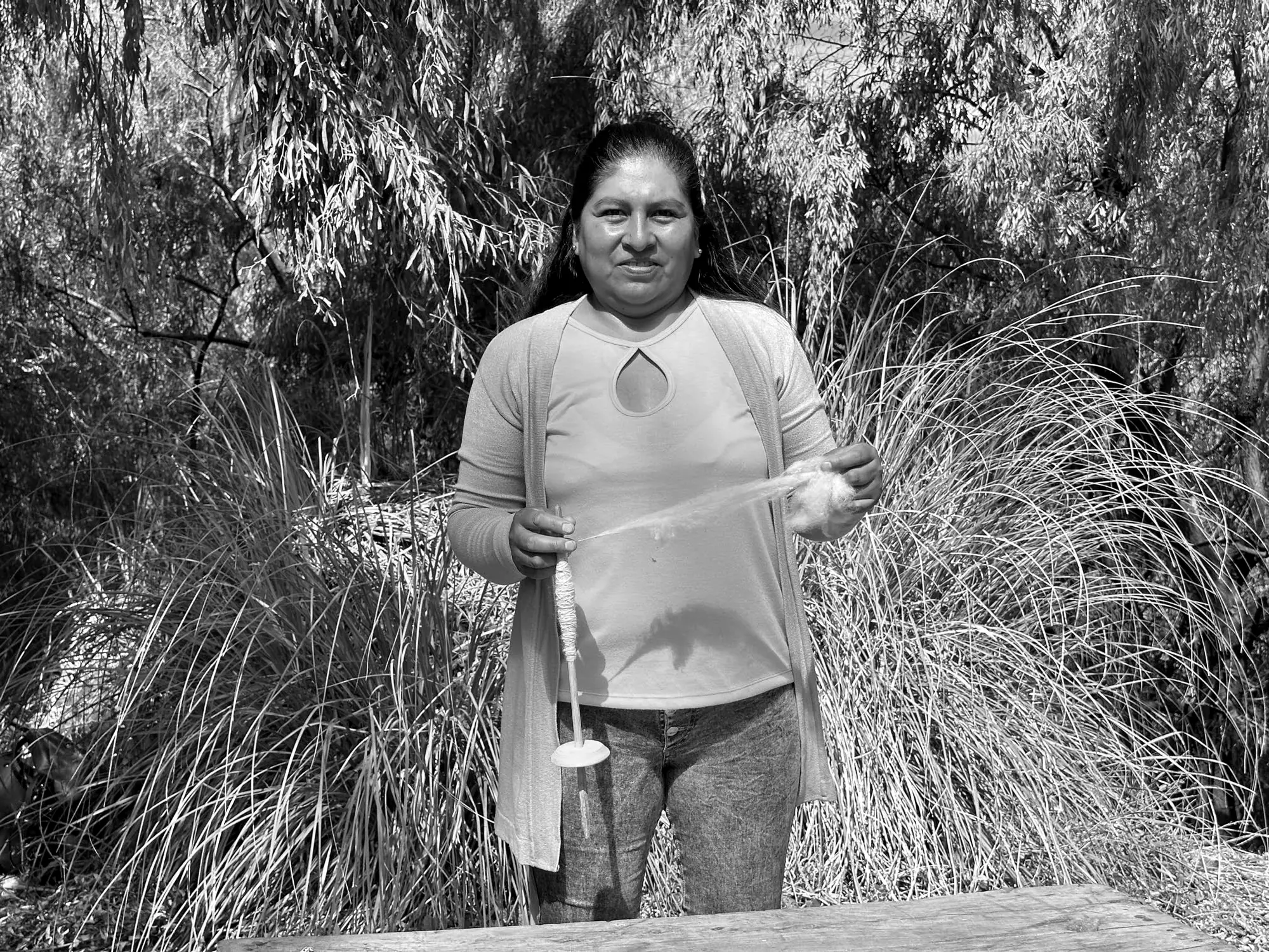 Artesana hilando lana con huso entre pastizales, en blanco y negro — Hilando Culturas, Argentina