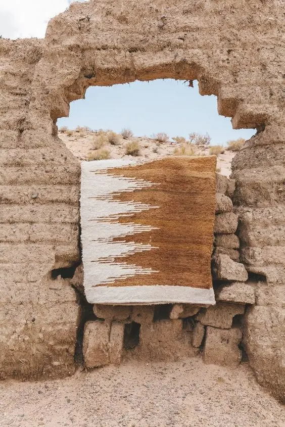Tapiz tejido a mano en tonos crudos y marrones, colgado en la abertura de un muro de adobe — Hilando Culturas